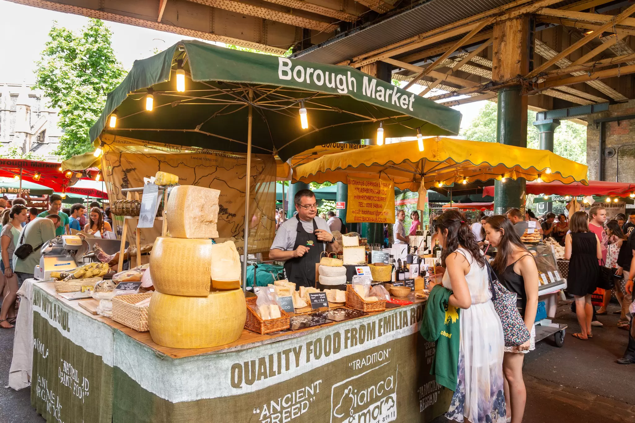 A cheese stall stacked with wheels of Parmesan under green umbrellas at Borough Market