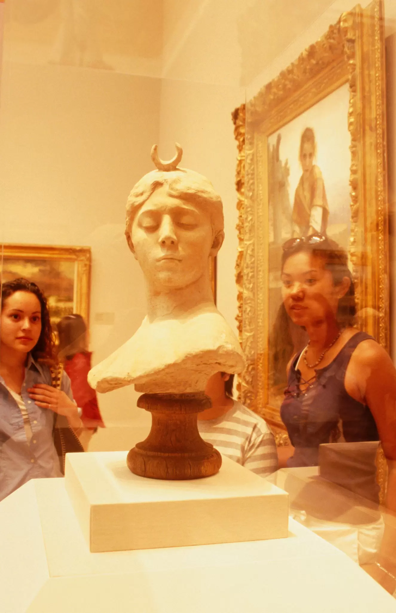 Visitors look at art displayed at the Palace of Legion of Honor in San Francisco. The art is of a bust of a woman's head, and is in a glass display cabinet.