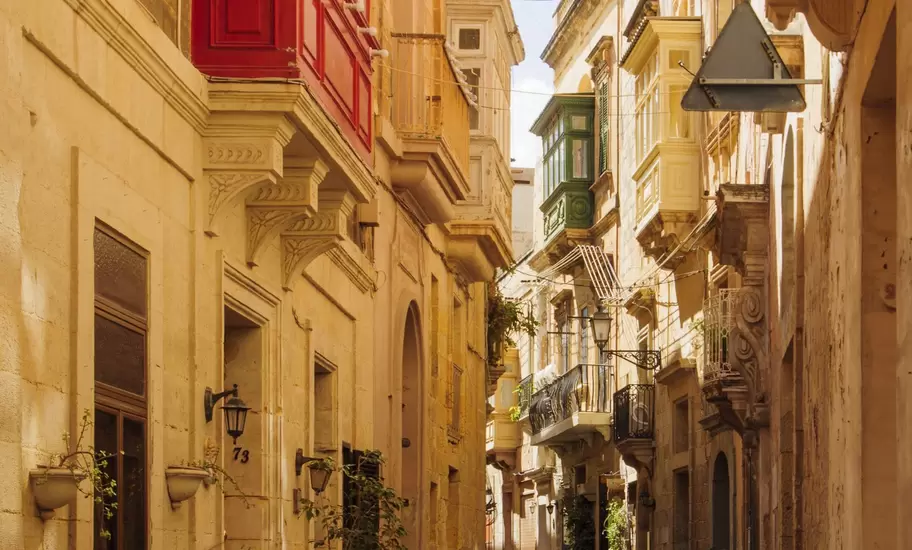 Narrow limestone street in Vittoriosa (Birgu), Malta, with red and green enclosed wooden balconies, lamps and potted plants