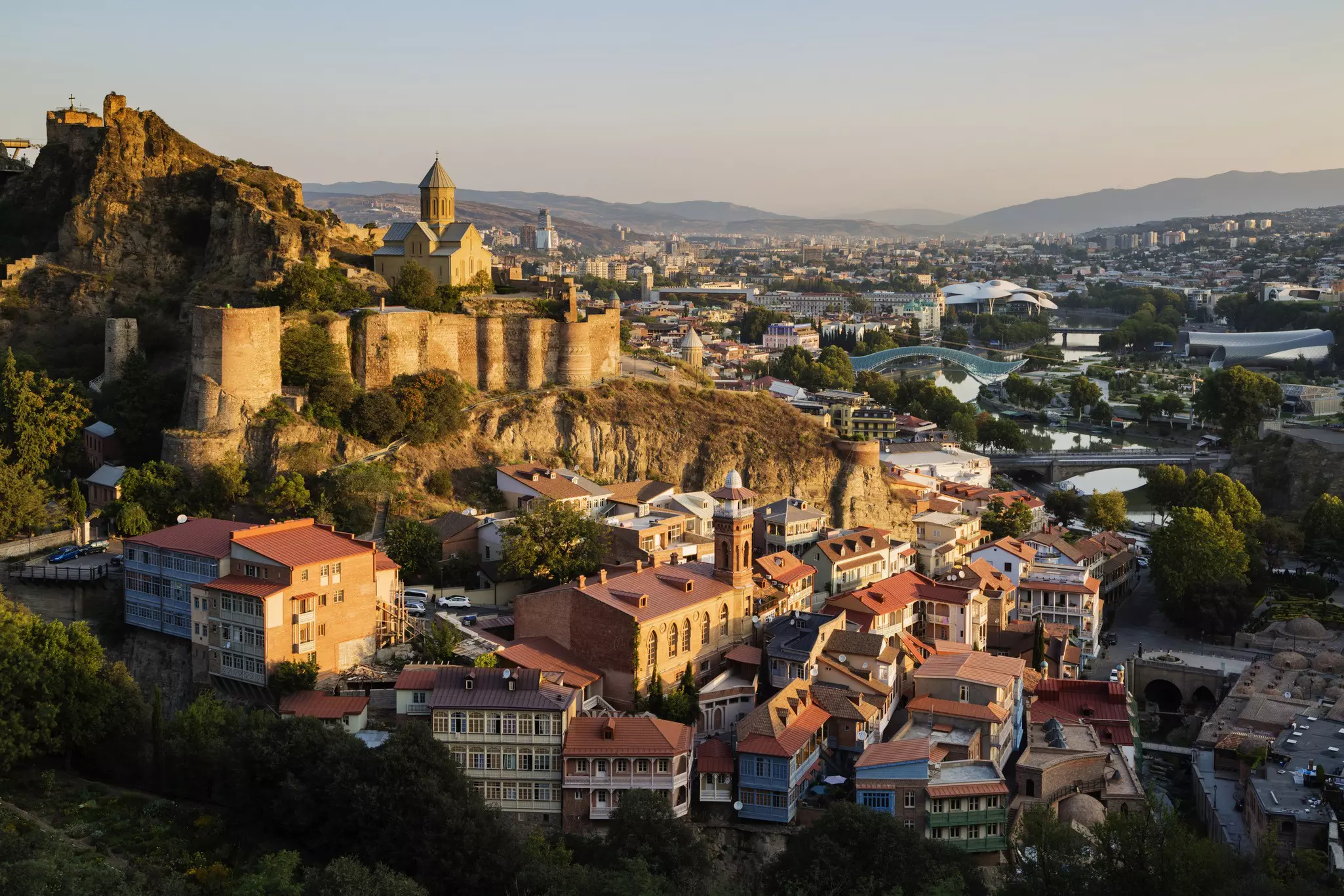 An aerial view of a historic fortress on a hill and large city in the valley below at dusk.