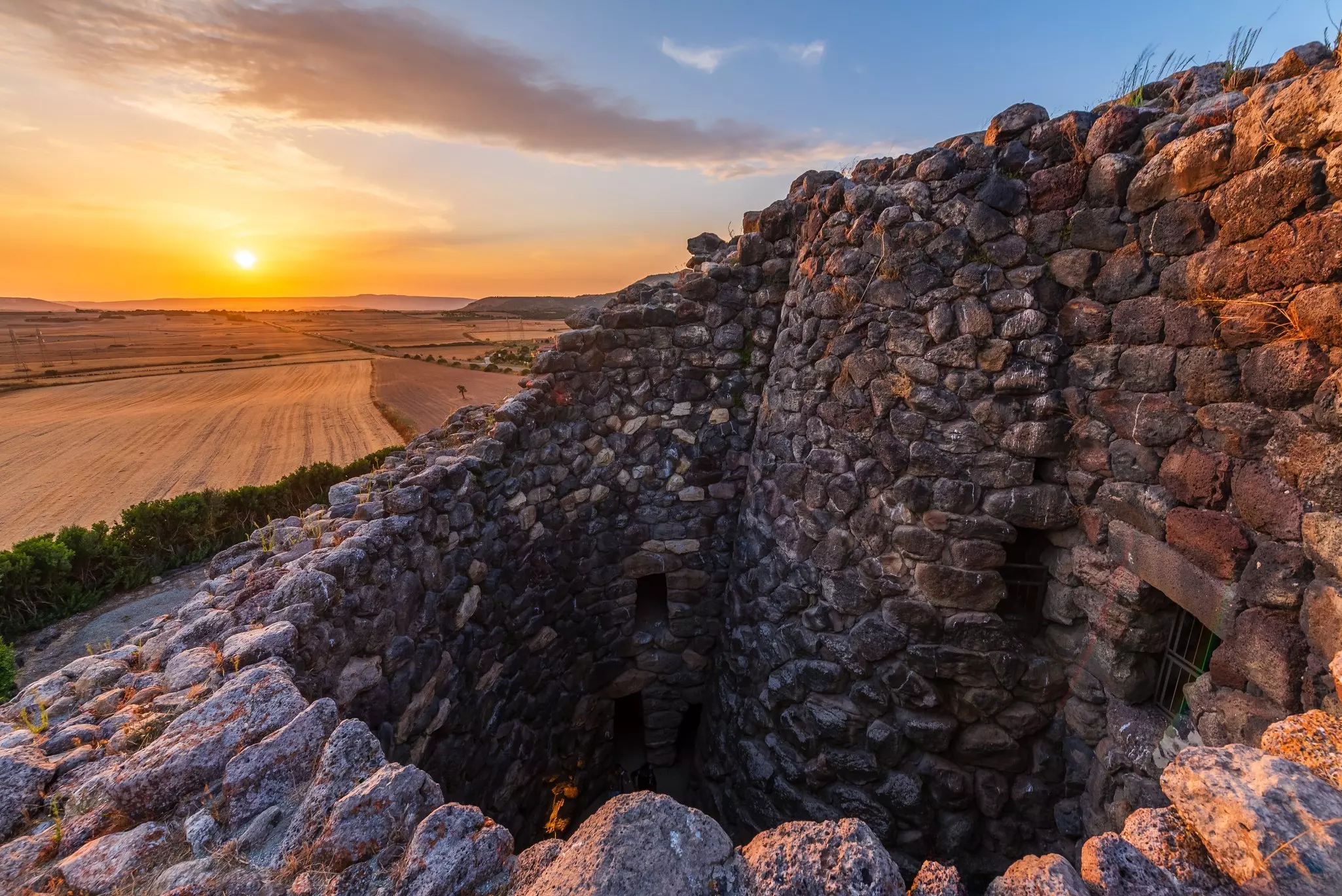Nuraghe Su Nuraxi, the ruins of early settlements, with a golden sun going down in the background