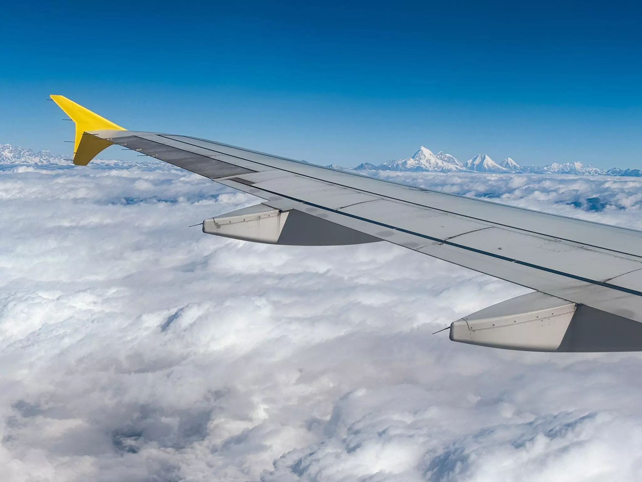 A snowy peak is visible above the clouds, as shot from the window of an airplane.