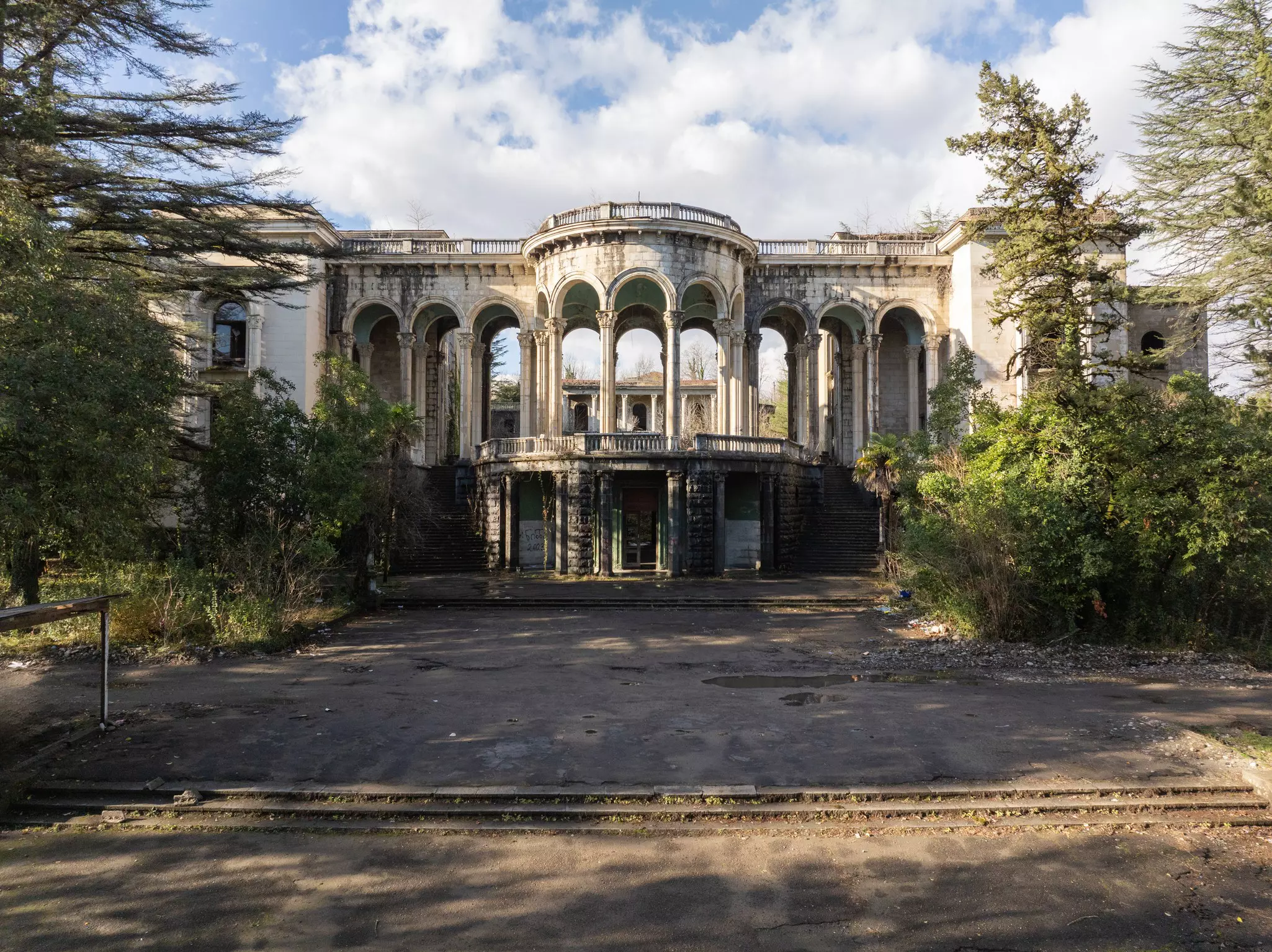 A large abandoned building in a state of disrepair, with a curved columned facade.
