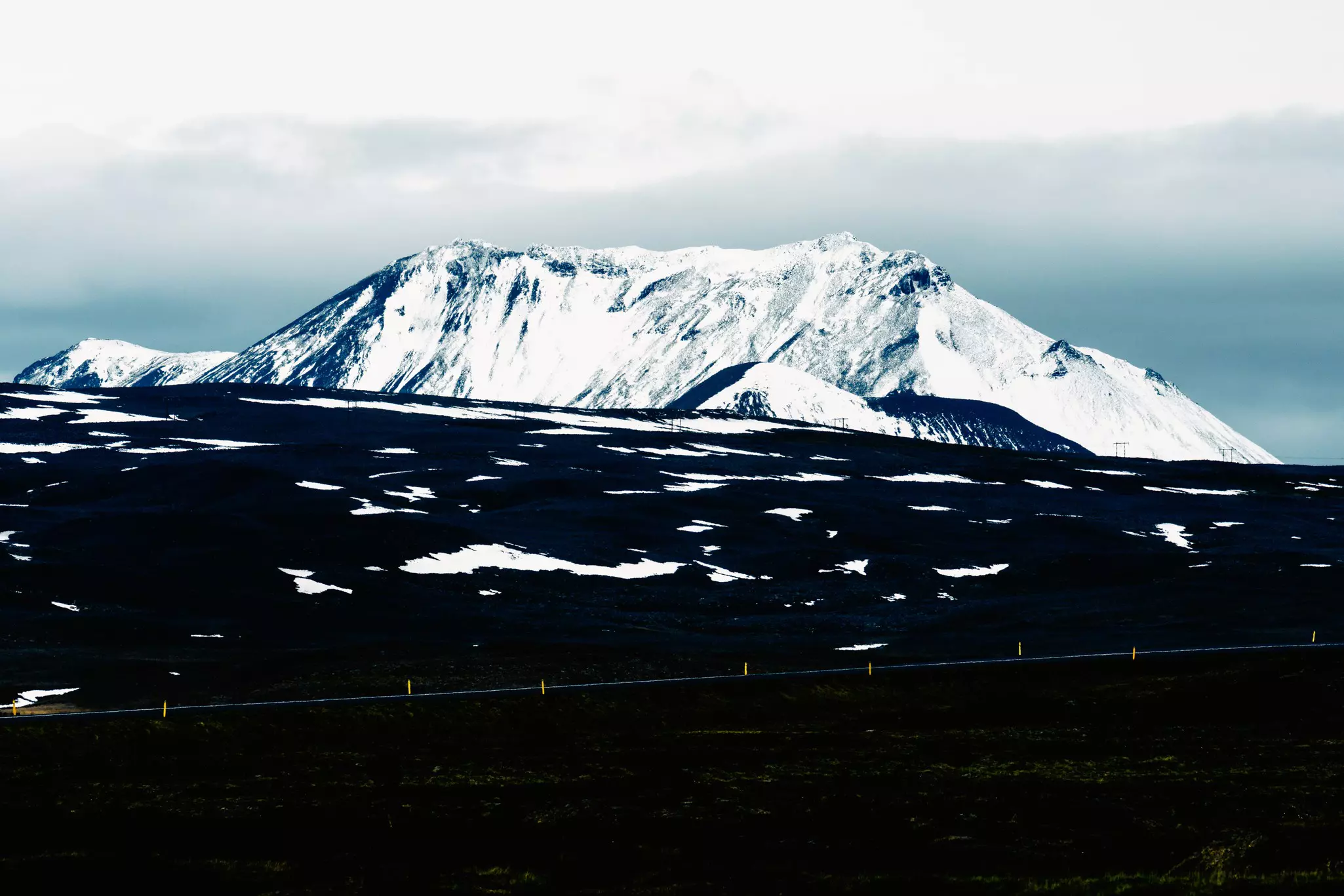 A large icecapped mountain over a black sand landscape