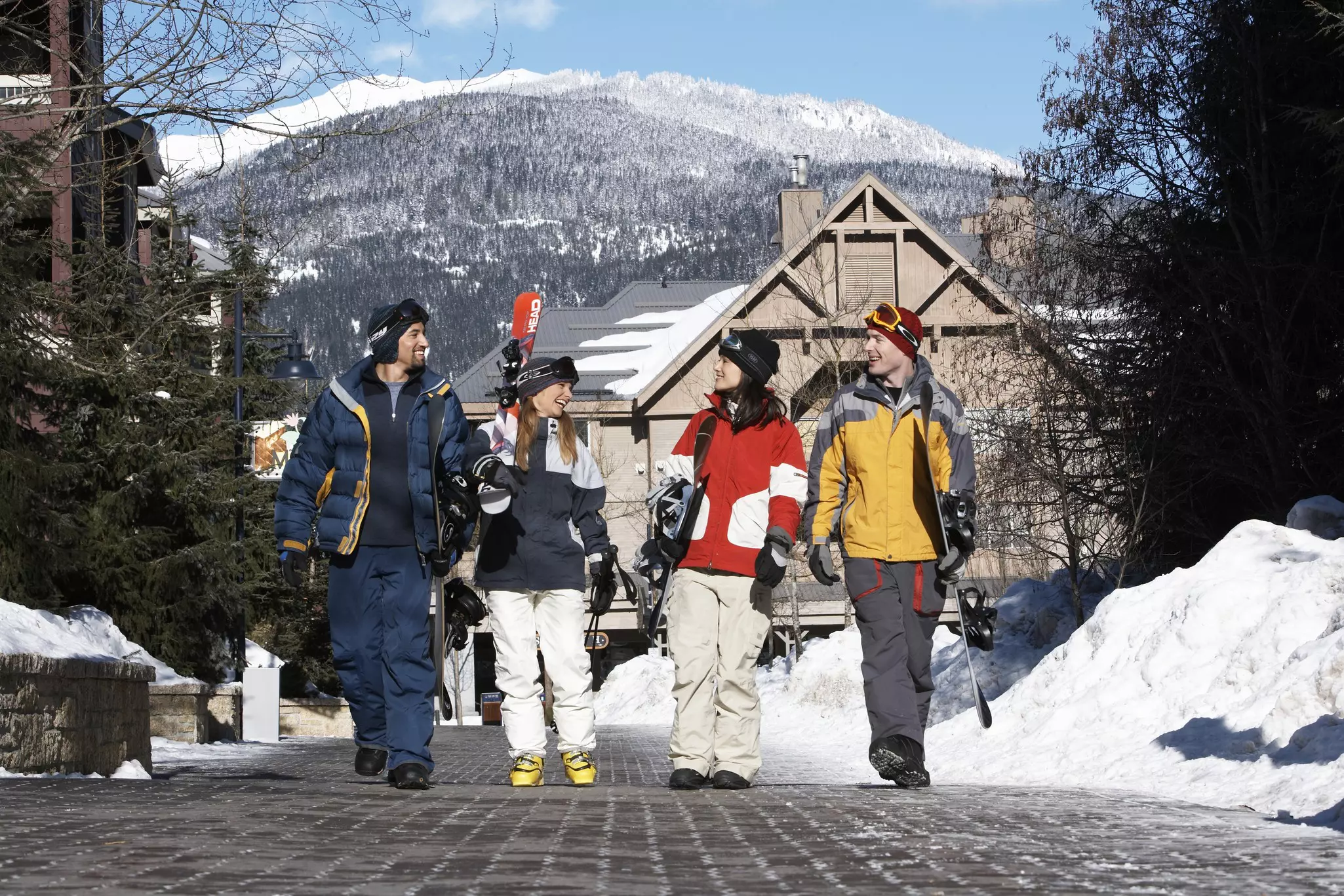 Adults walking along together chatting while carrying skis and snowboards
