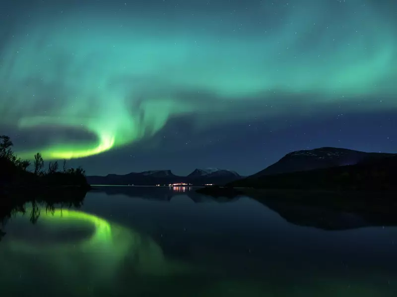 Streaks of green in the sky over a calm lake at night.