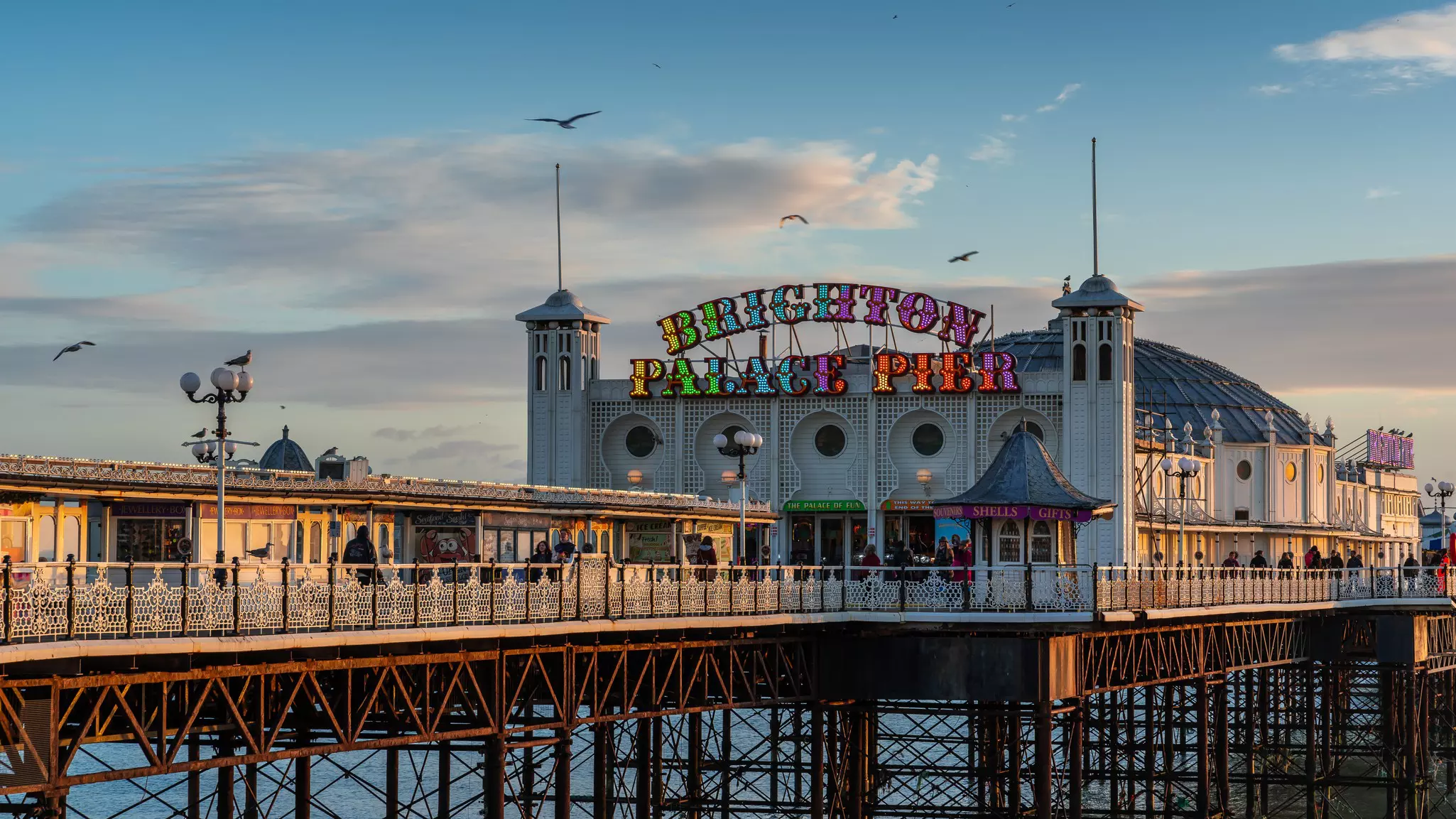 Image of a long pier with a brightly colored lighted sign reading "Brighton Palace Pier" on a stone building.