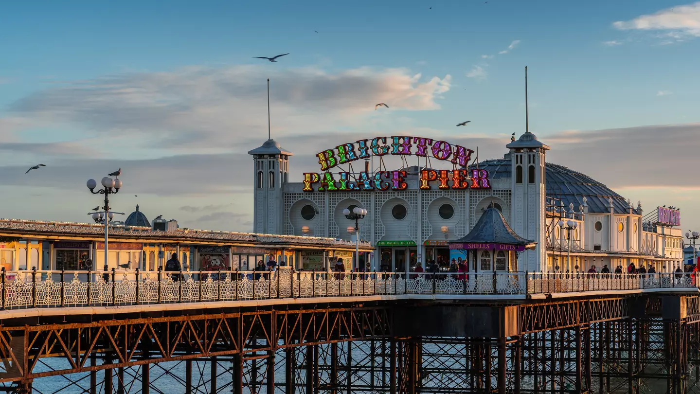 Image of a long pier with a brightly colored lighted sign reading "Brighton Palace Pier" on a stone building.