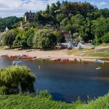 Canoes and swimmers on the Dordogne River beside a stone bridge below the hillside village of Limeuil, France