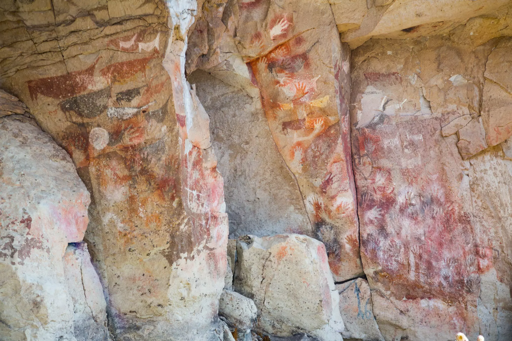 Reddish rock drawings and handprints in on whitish stone caves.