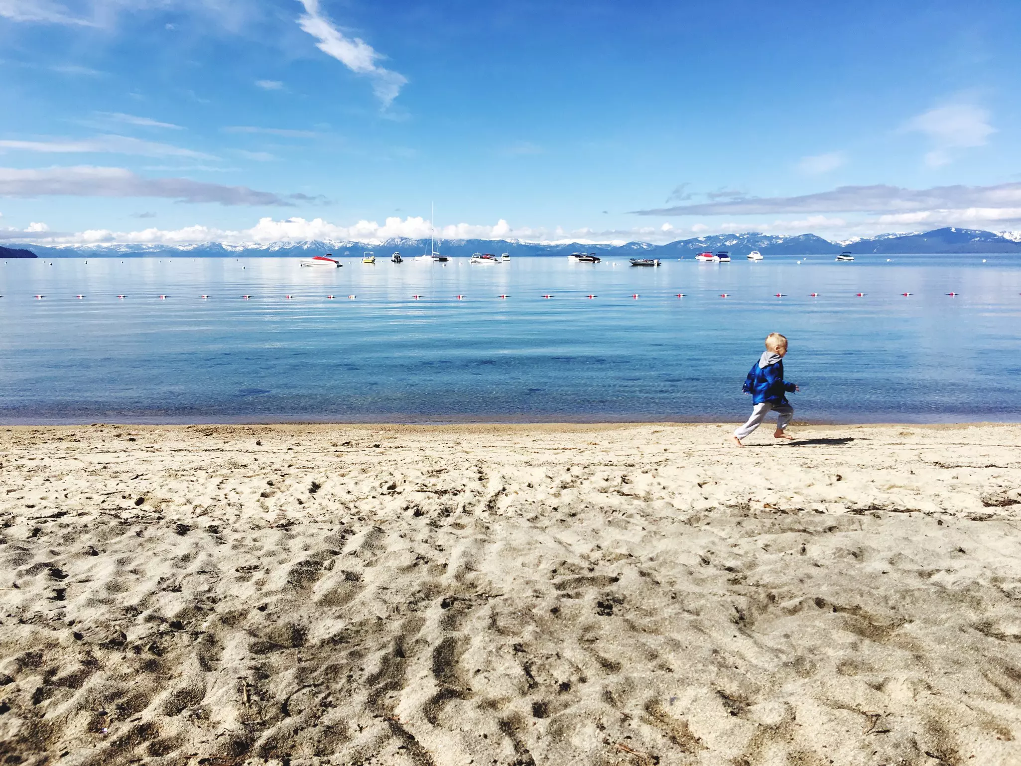 A small child runs along a beach beside a lake