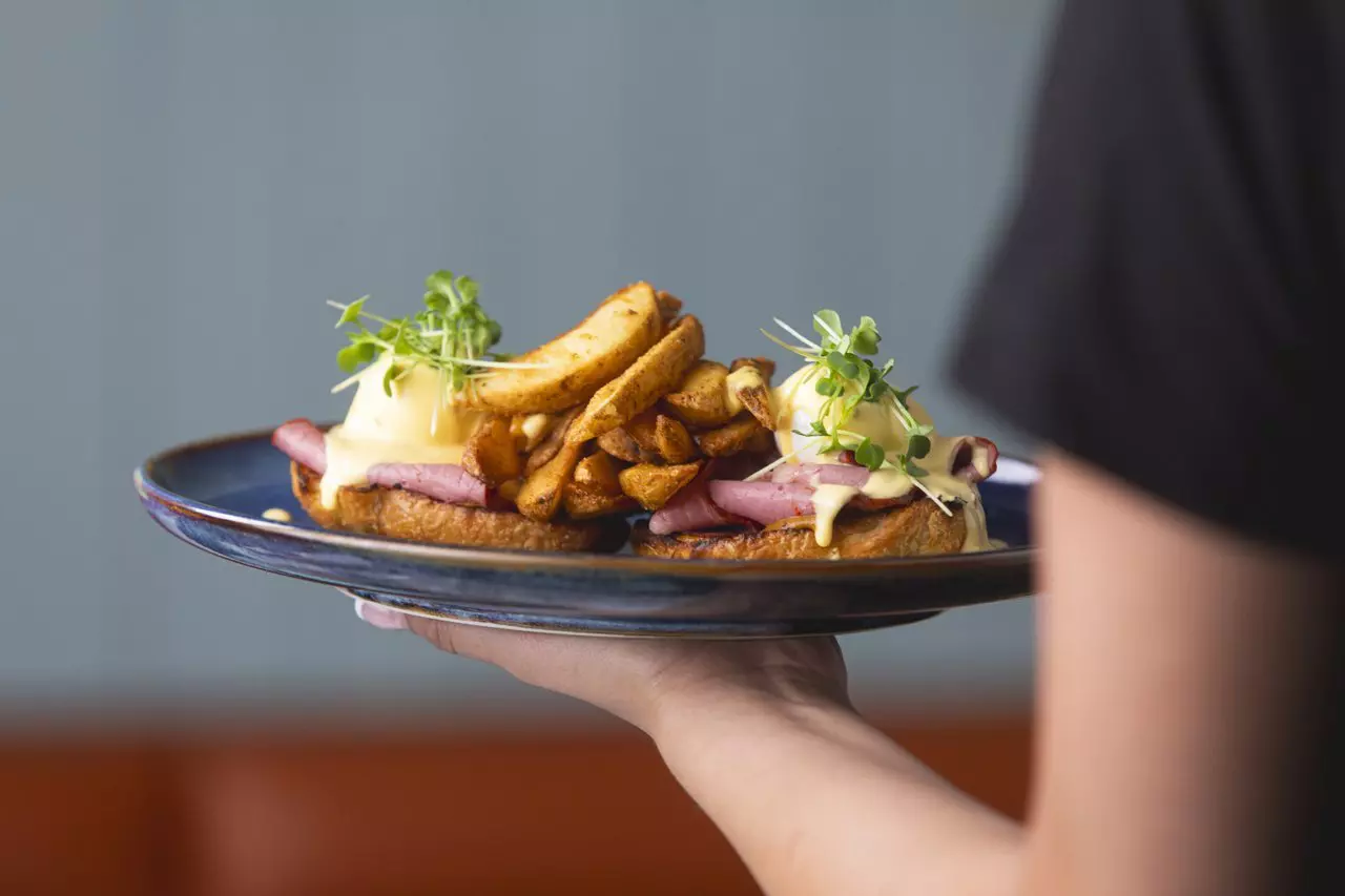 A server holds a plate of food including fries and eggs covered in sauce.