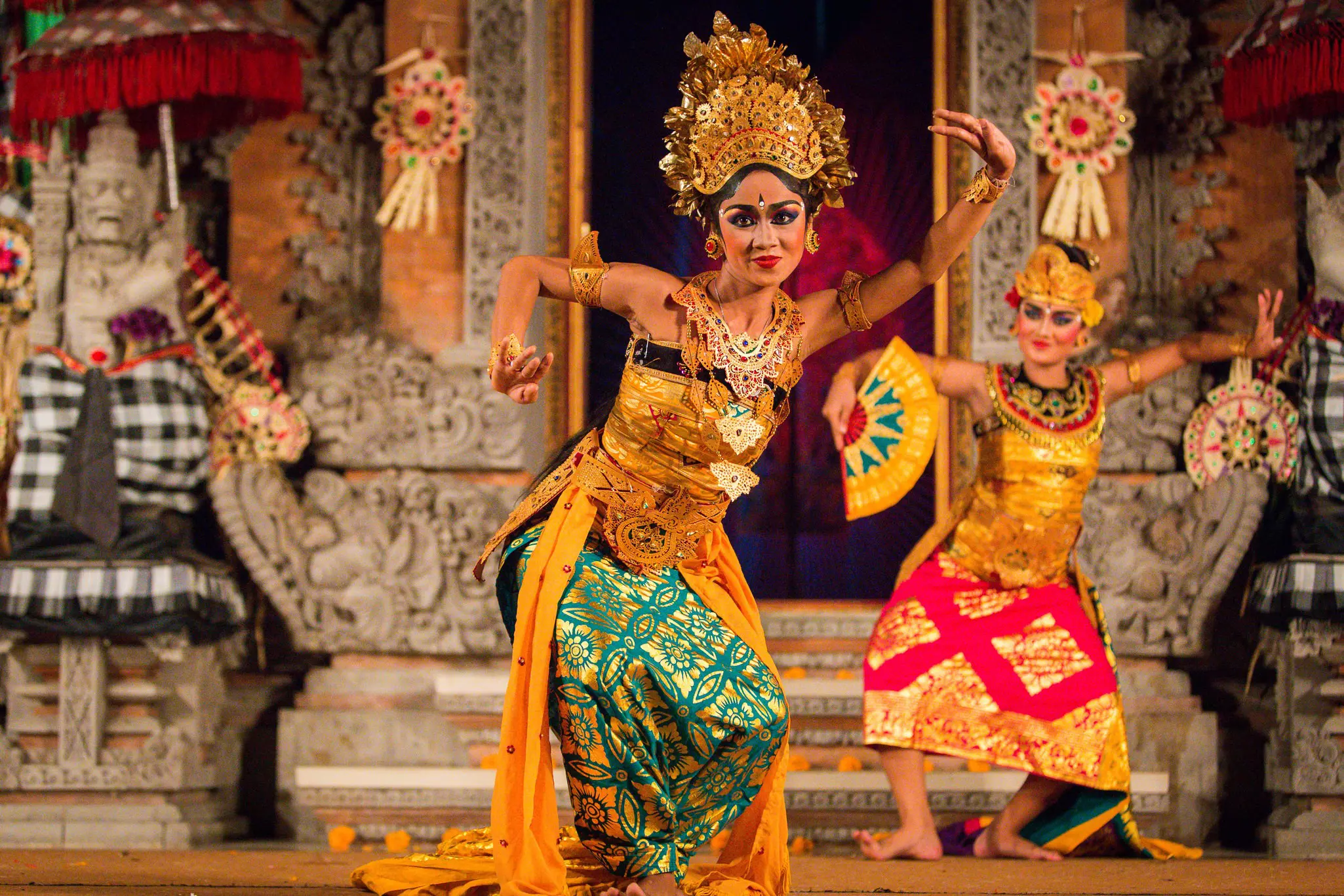 Two women in golden heavily decorated clothes and headdresses perform a dance.
