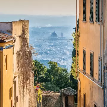 A narrow road between yellow houses in Fiesole, Italy, framing a distant view of Florence's cathedral dome.