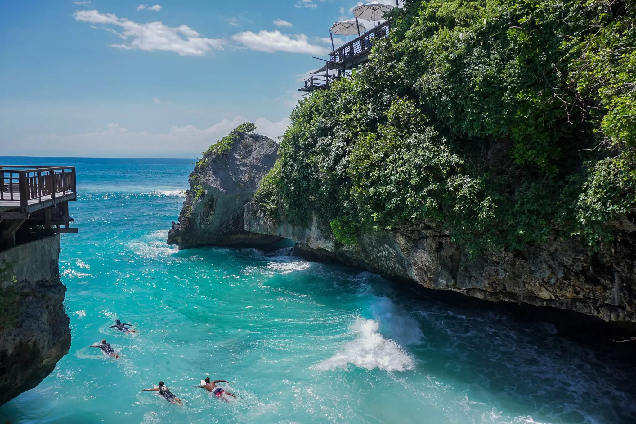 Looking down on a tropical cove where people are swimming. A rock formation looms over the cove.