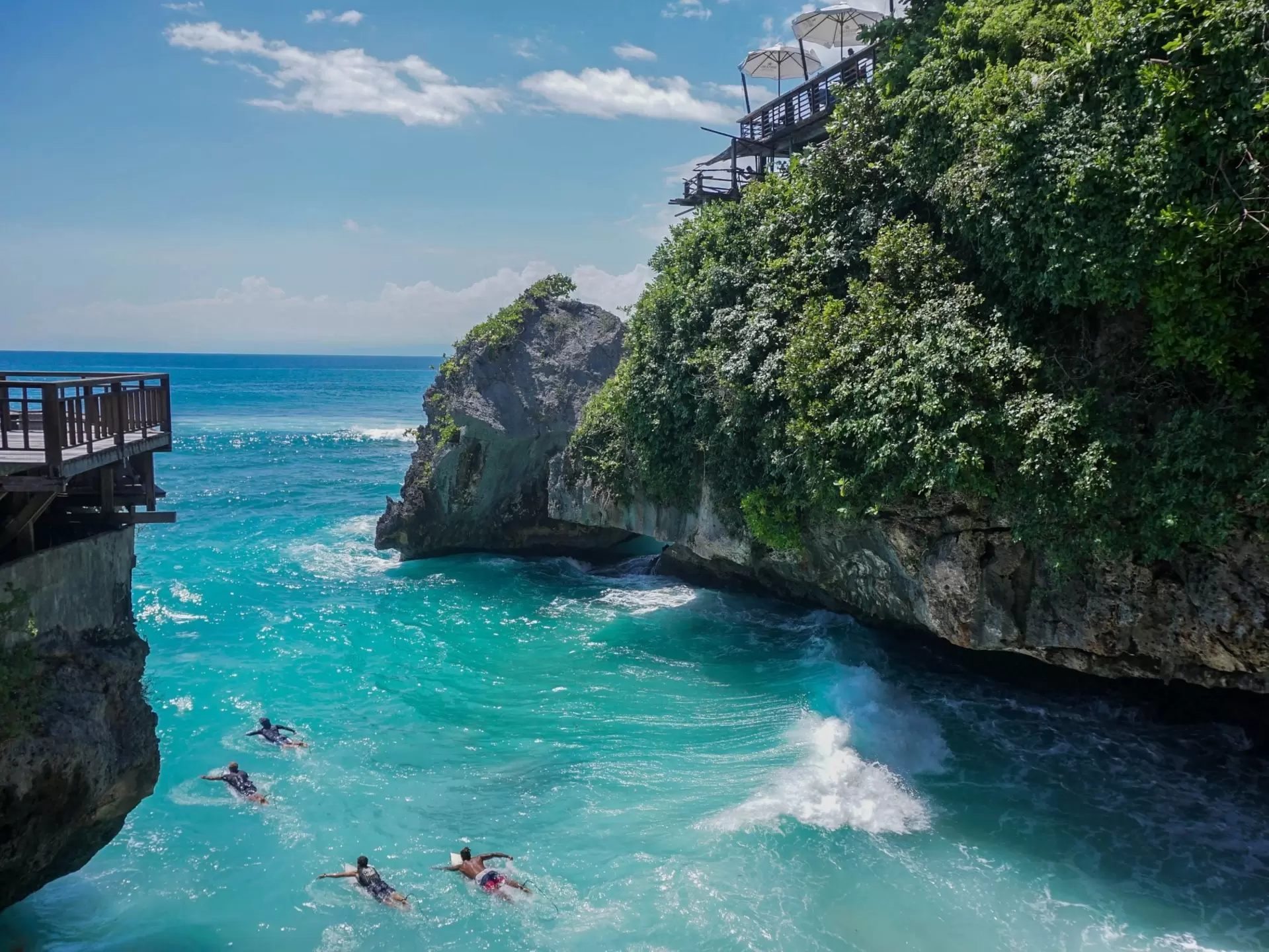 Four people swimming in turquois waters near a cliff