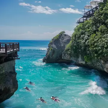 Four people swimming in turquois waters near a cliff
