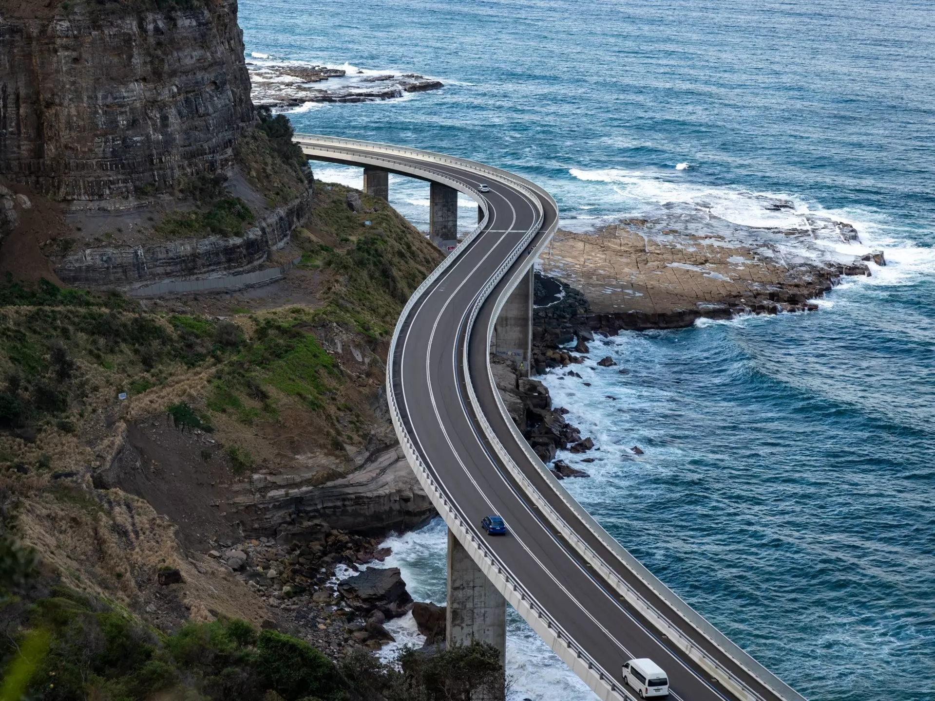 A windy highway causeway hugs cliffs above the ocean