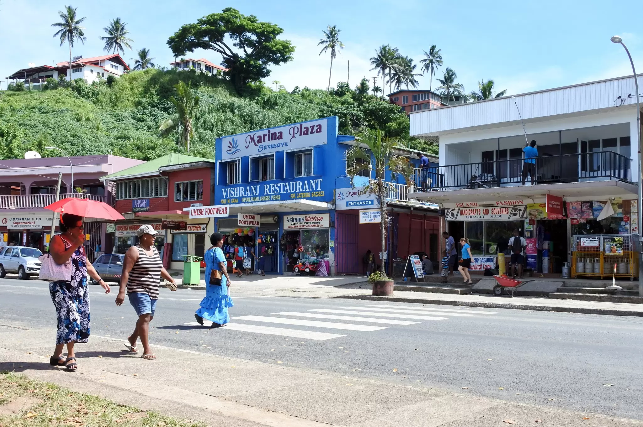 People walking along and crossing a main road lined with colorful shops and restaurants