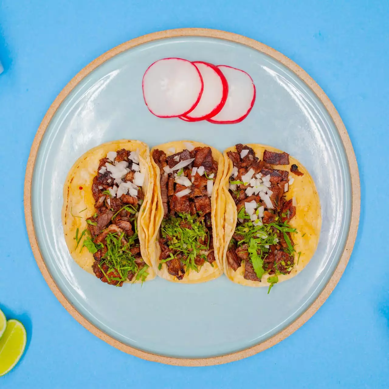 Three tacos on a white plate over a blue table