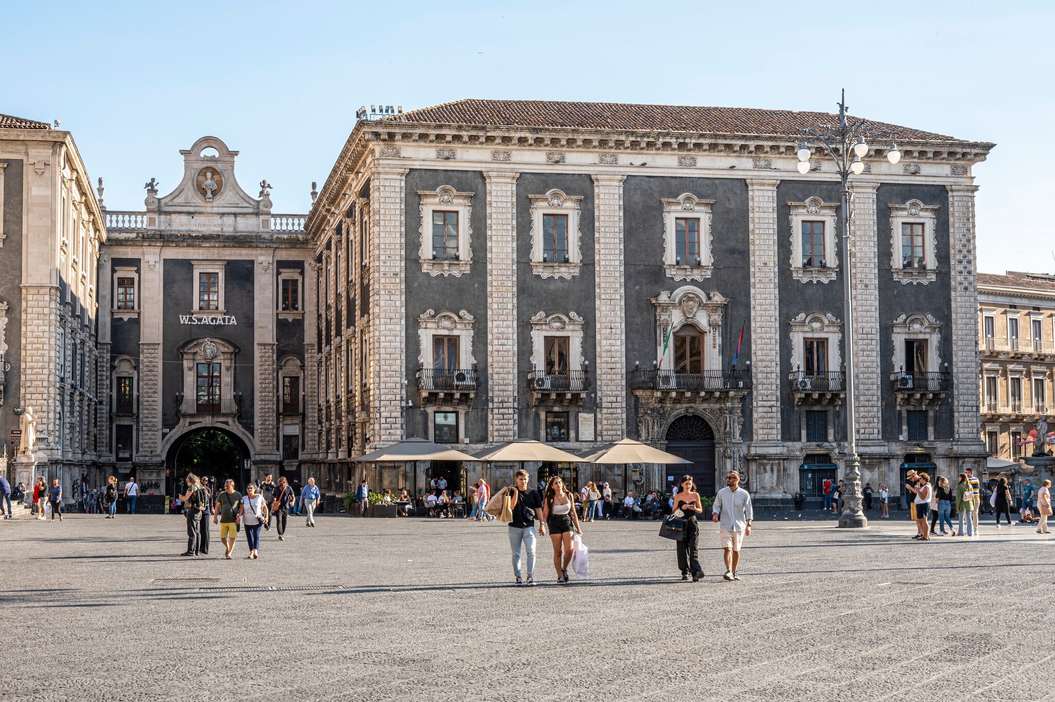 Duomo Square in Catania, with historic buildings surrounded by tourists on a sunny day.