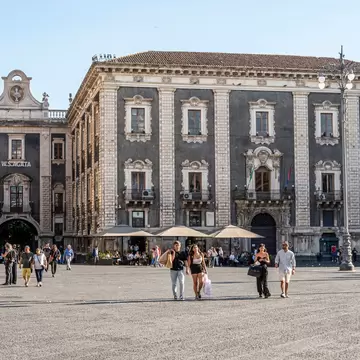 Duomo Square in Catania, with historic buildings surrounded by tourists on a sunny day.