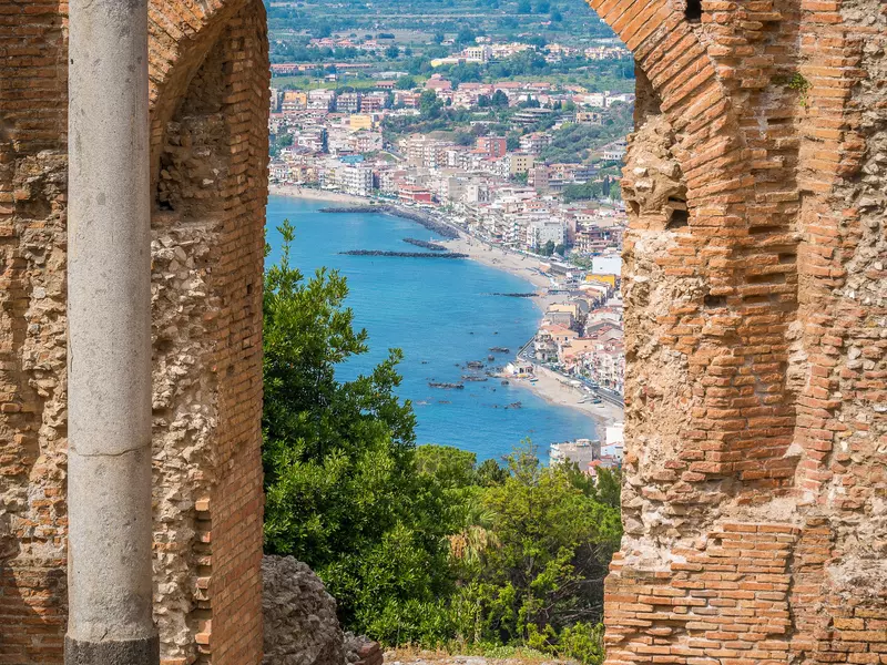 A view of a town by the sea through an archway at an ancient ruin in Italy. 