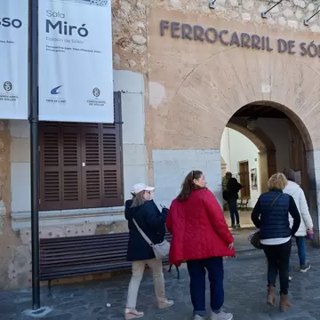 Visitors walking through the stone archway of the Ferrocarril de Sóller station beside a Sala Miró banner