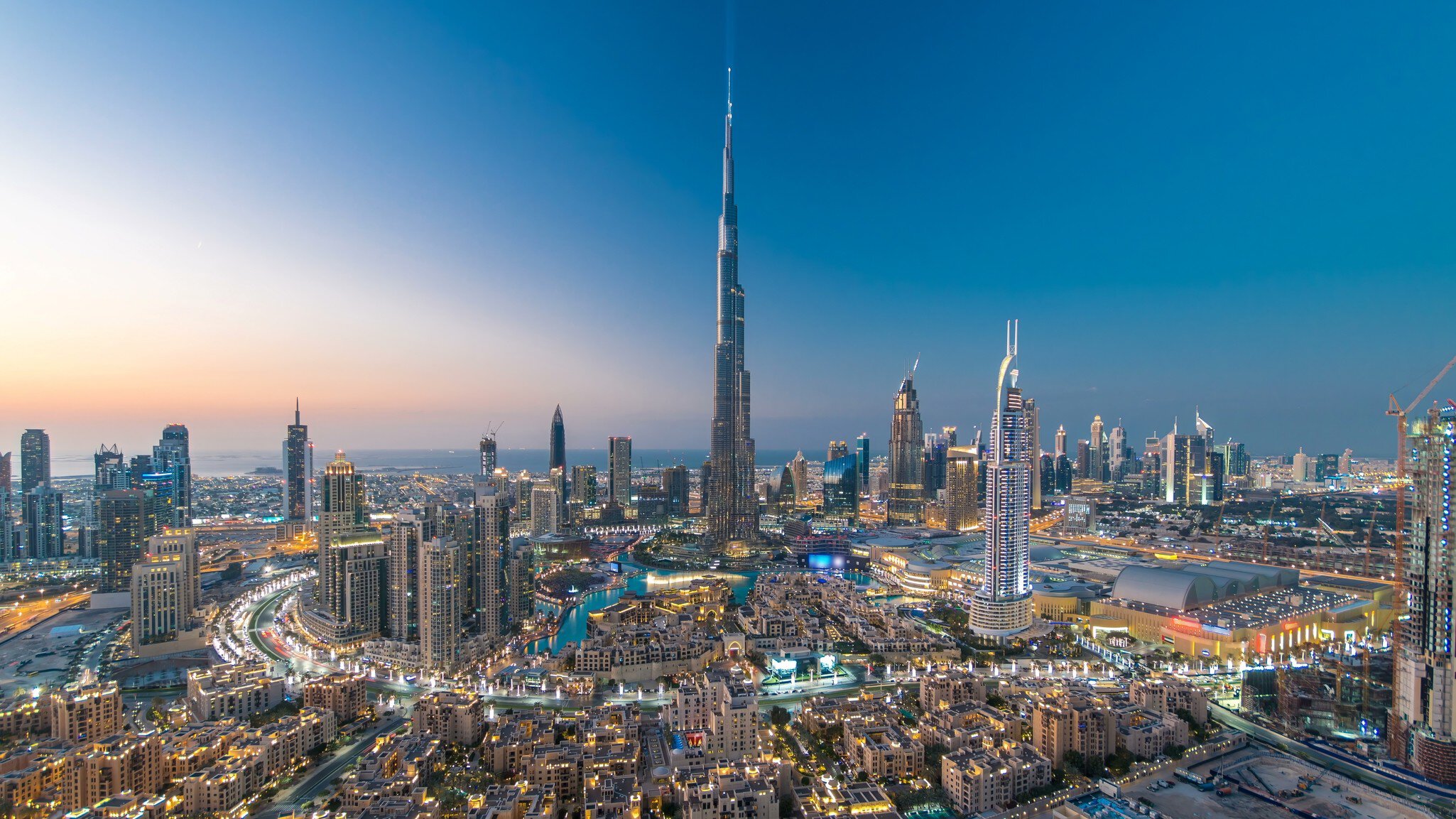 Aerial view of a dense city at dusk with a tapering supertall tower.