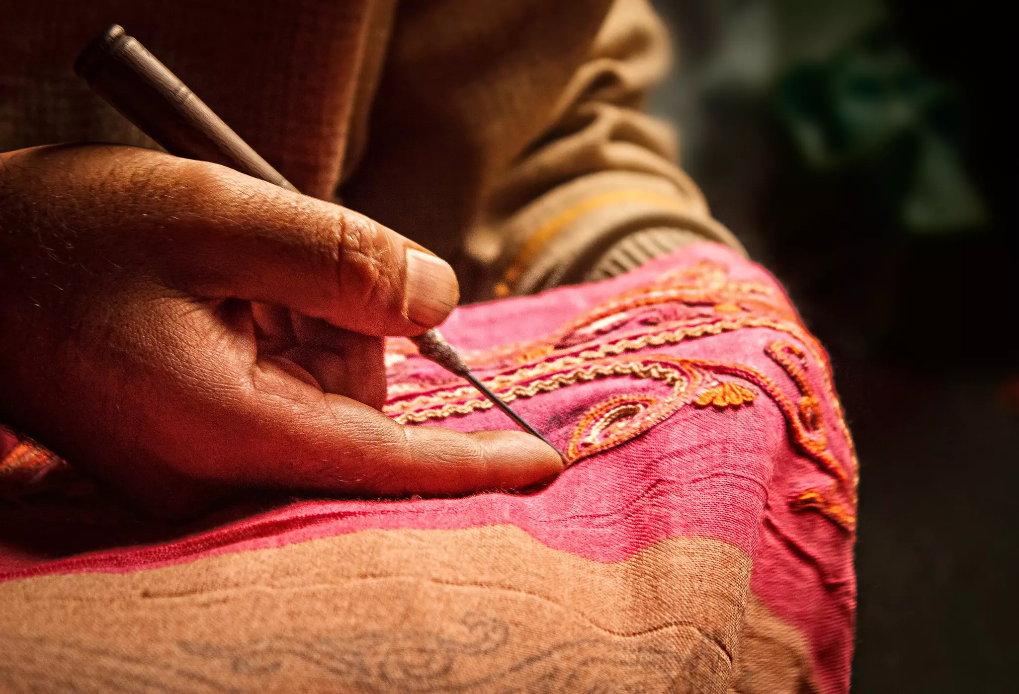Kashmiri man uses an Aar needle to form Aari Embroidery on a pink scarf, a traditional form of embroidery from Kashmir.