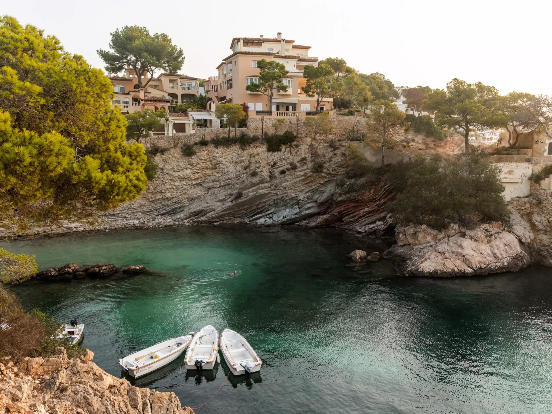 Small boats anchored in a secluded cove surrounded by rocky cliffs and greenery.