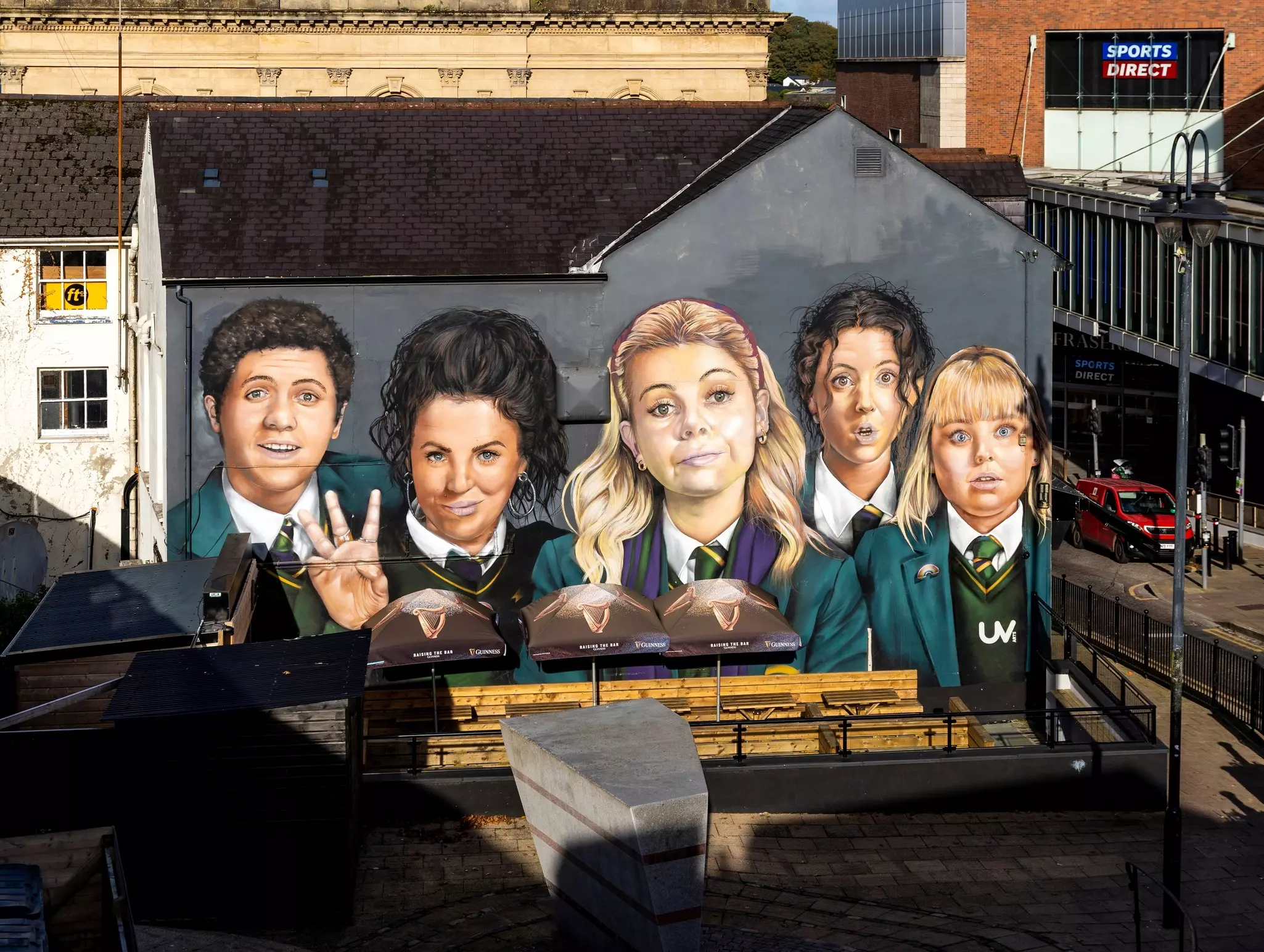 An overhead shot of a huge painted wall mural in a city depicting five schoolgirls.