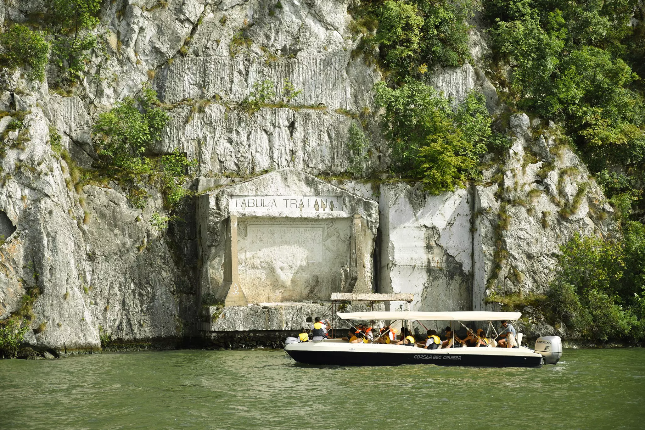 a sightseeing boat on a green river with huge rocks behind