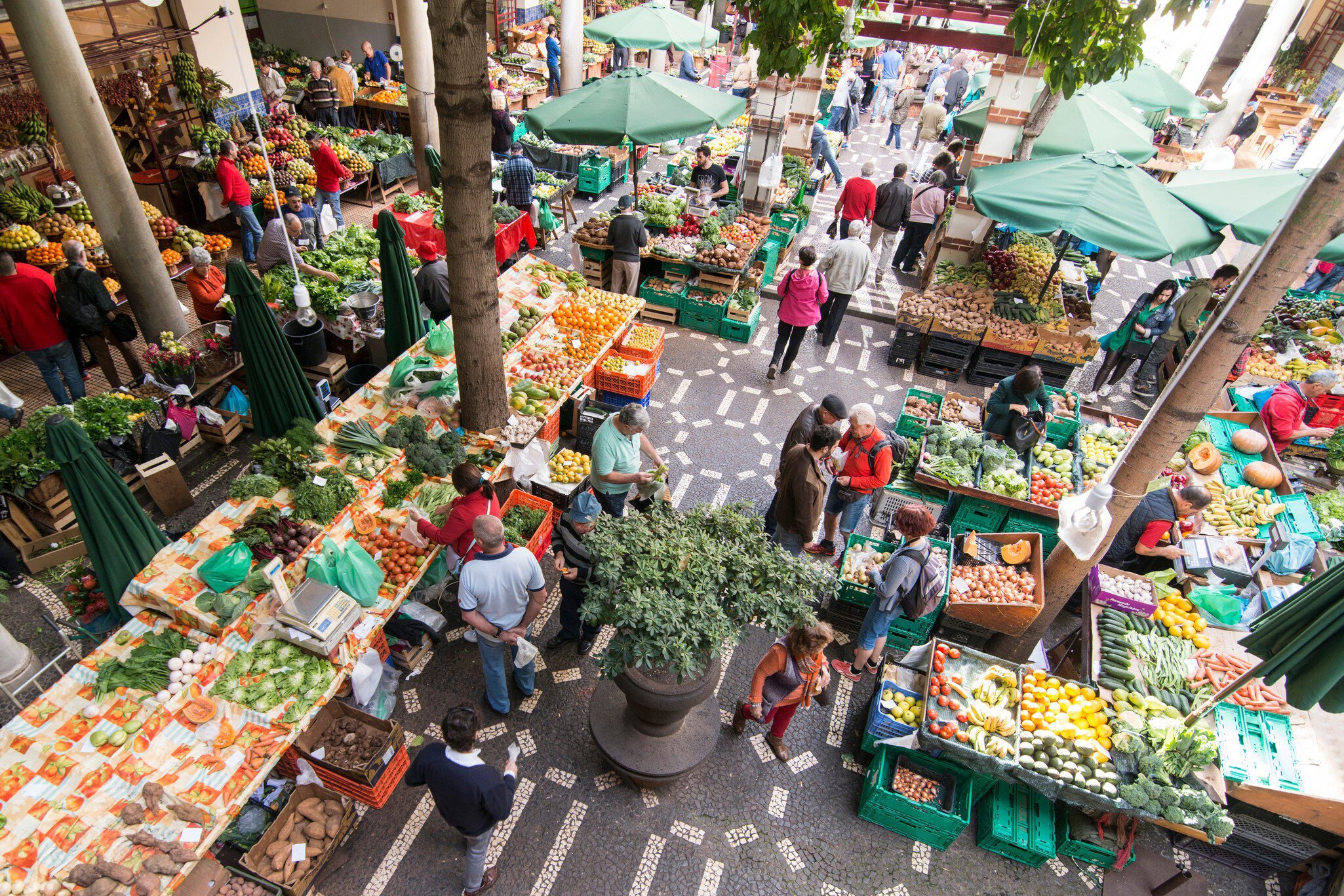 Looking down on a covered market courtyard of fruit and vegetable stalls under green parasols.