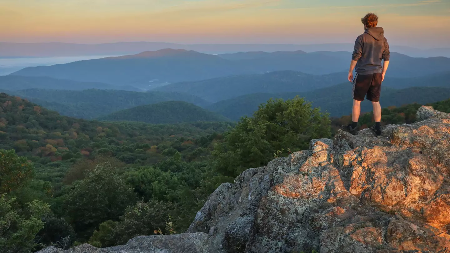 A male hiker stands on top of Bearfence Mountain at sunset in Shenandoah National Park