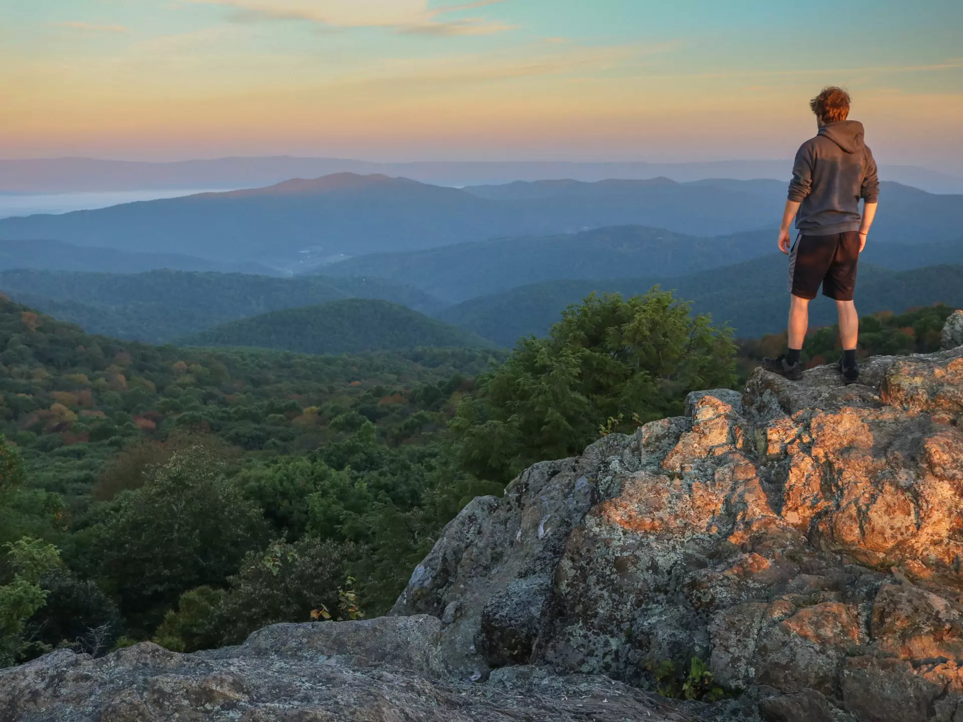 A male hiker stands on top of Bearfence Mountain at sunset in Shenandoah National Park