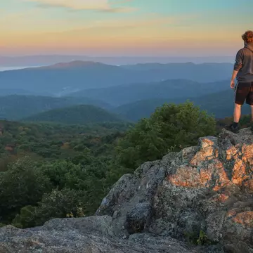 A male hiker stands on top of Bearfence Mountain at sunset in Shenandoah National Park