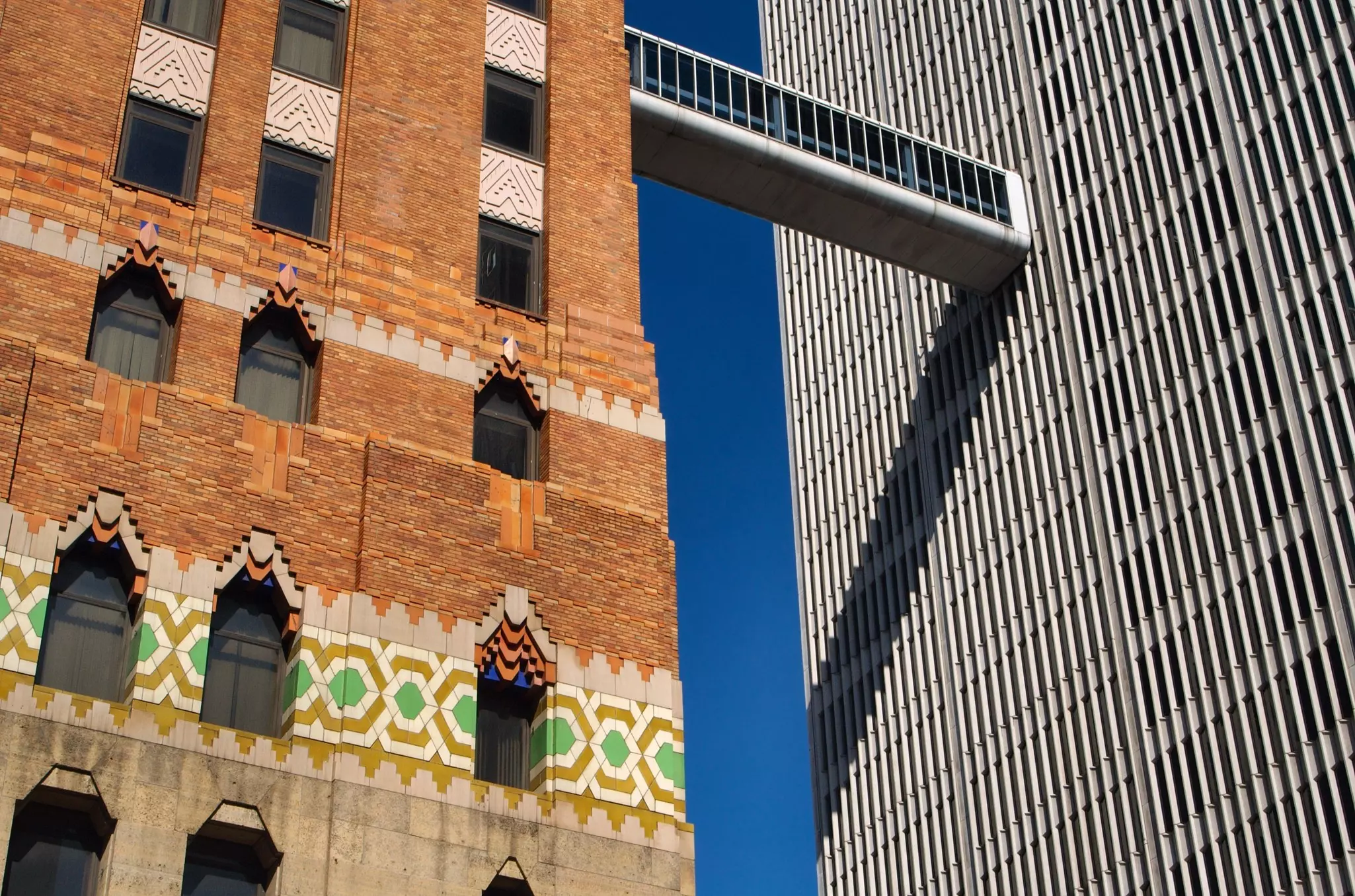 An Art Deco building connected to a modern building by a high-story covered walkway to a modern skyscraper with a sliver of blue sky showing in between the two buildings.