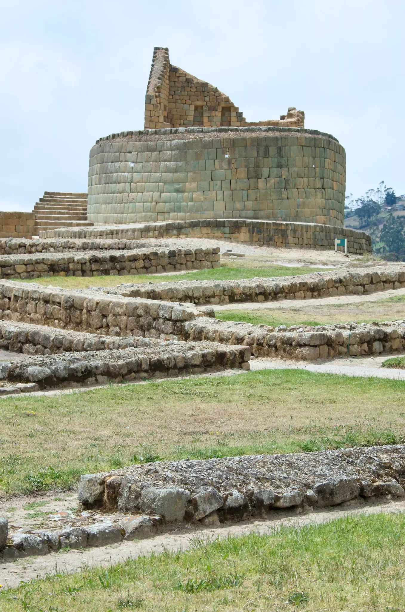 Low stone walls cross areas of grass in front of a circular stone structure in Ecuador.