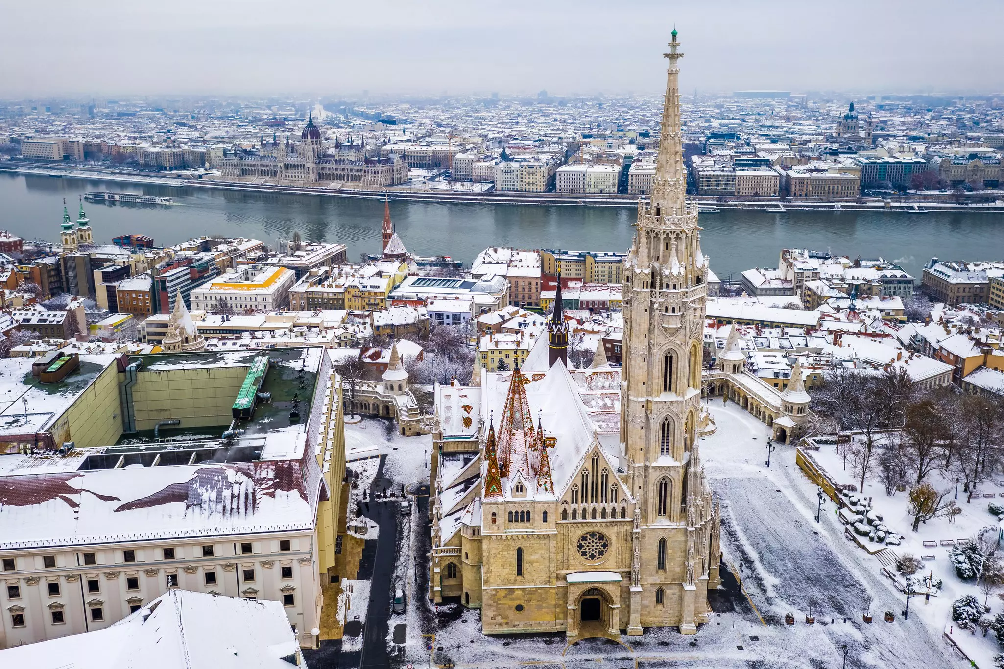 An aerial view of a snow-covered church and other monuments in a city, with a river in the distance.