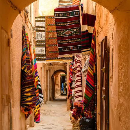 Colorful fabrics are displayed on walls seen through an archway in an Algerian town.