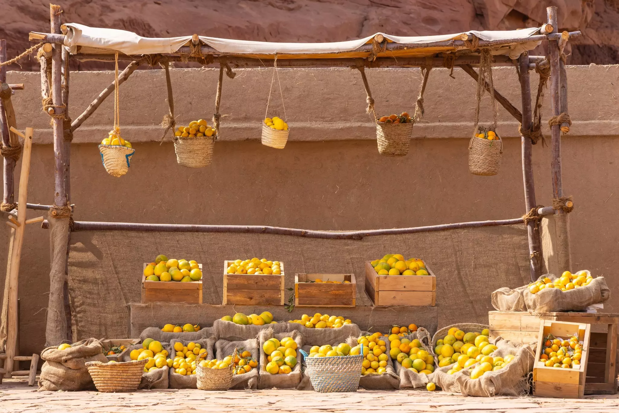 Baskets of oranges hang from a pole; crates of oranges are underneath.