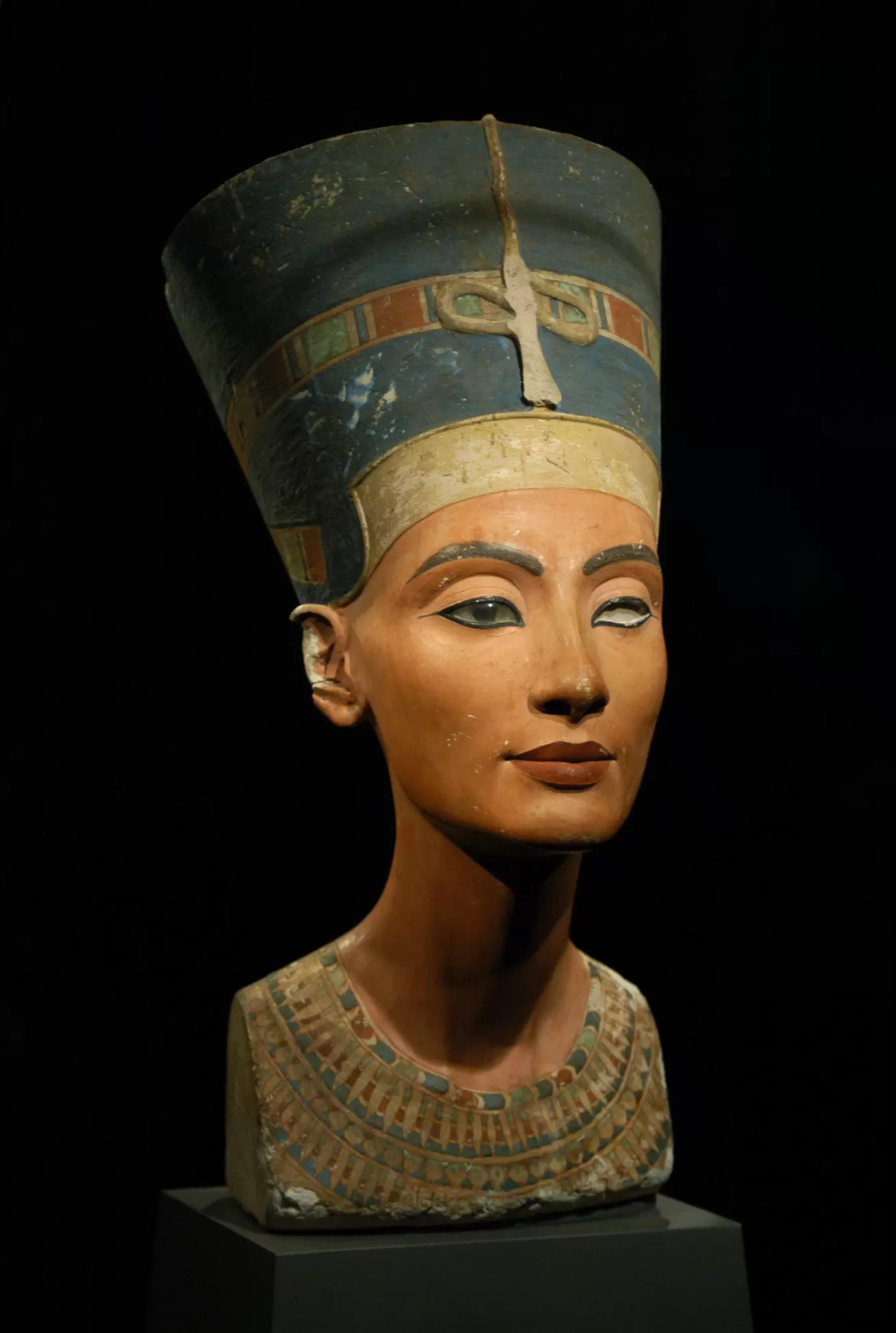 An ancient sculpture of a woman from the chest upwards. She wears a tall hat.