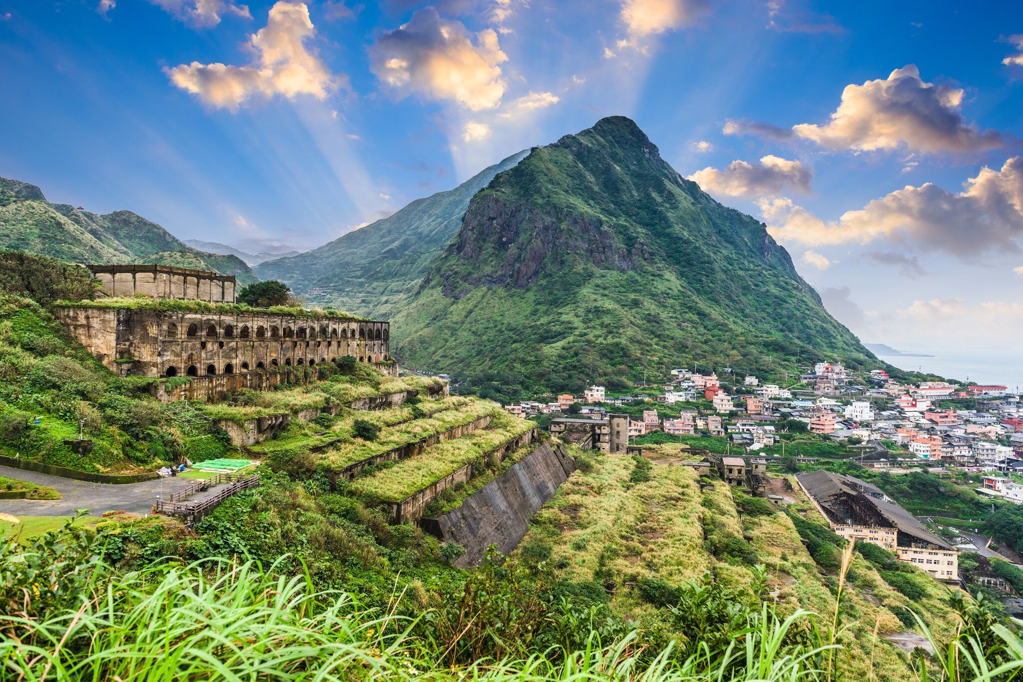Stone 13 Levels terraced ruins on a green grassy hill, with a lush green mountain in the background on a sunny day. 