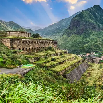 Stone 13 Levels terraced ruins on a green grassy hill, with a lush green mountain in the background on a sunny day. 