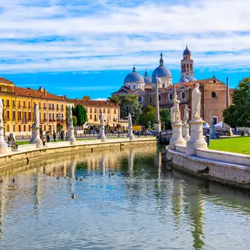 Statues line the canal at Prato della Valle square with the Basilica Santa Giustina (Abbey of Santa Giustina) in the background.