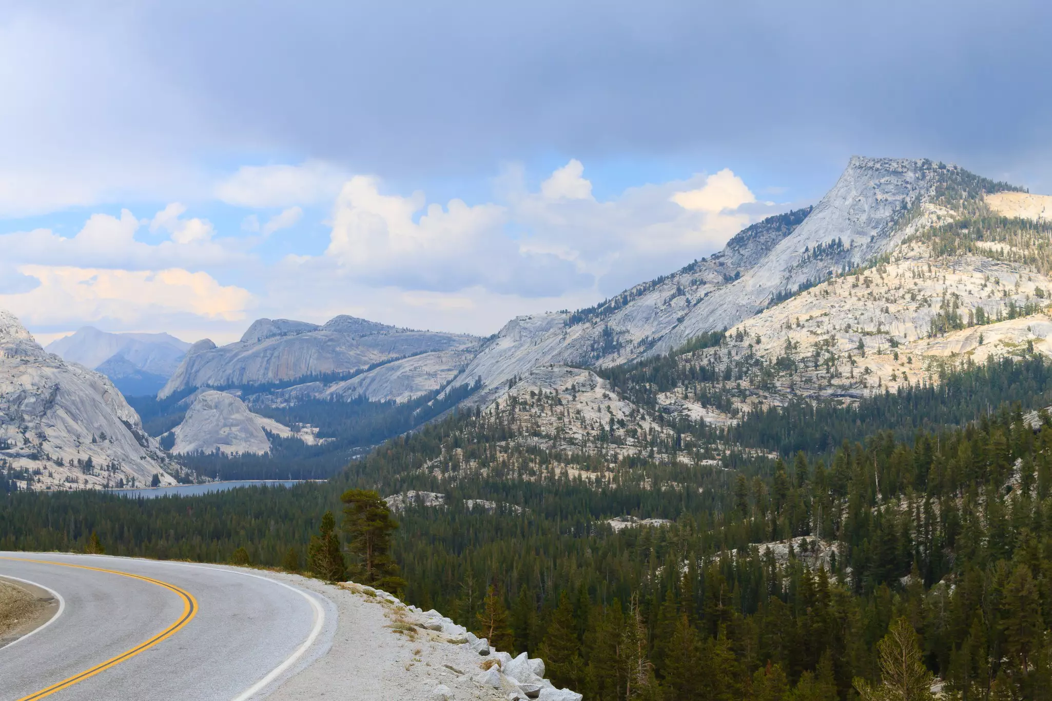 A panoramic view of mountains from a road. Pines cover the slopes of the mountains.