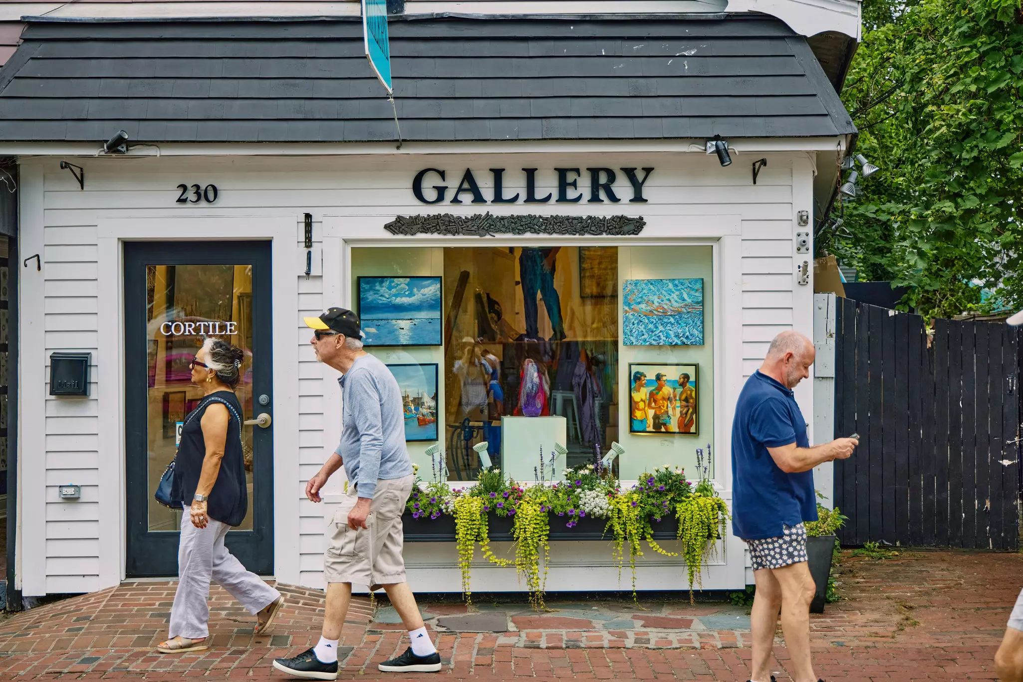 People walk on a sidewalk in front of an art gallery in small wood-front building.