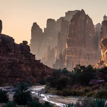 Sunset in a rock canyon with two tiny figures by a a small stream.