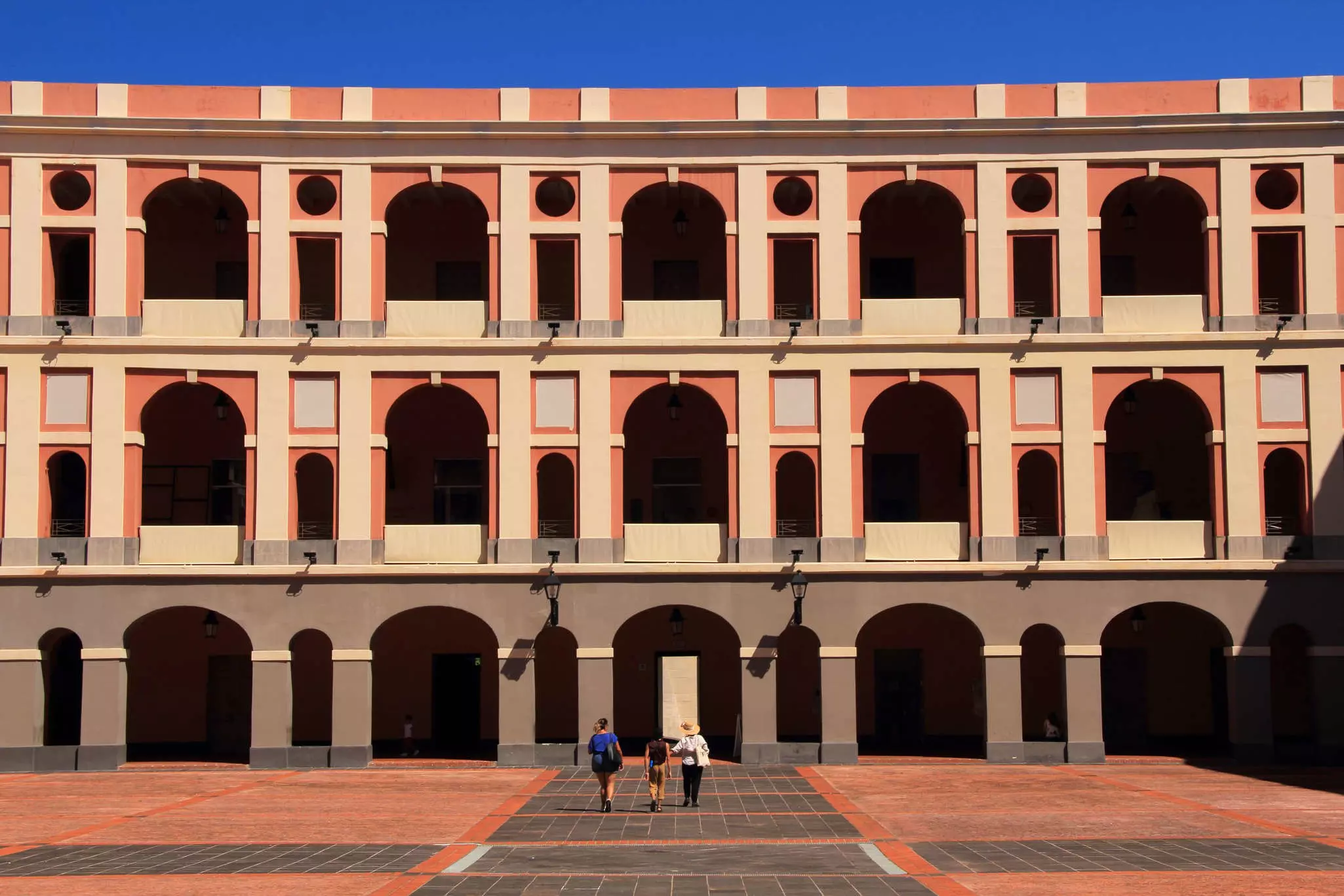 People walking toward the Museo de las Américas in San Juan, Puerto Rico, a towering, three-story facade with rows of arches